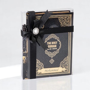 May include: A boxed set featuring a black Quran with gold filigree, a prayer bead, and a black ribbon with a pearl-centered embellishment. The Quran is labeled "THE HOLY QURAN Arabic - English" with the name "Mohammed" below.