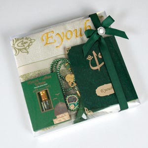 May include: A gift set containing a green prayer rug with gold embroidery, a green book, a green beaded rosary, and a small bottle. The set is wrapped in clear cellophane and tied with a green ribbon and a decorative jewel.