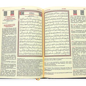 May include: An open book with Arabic script and French translation. The pages are cream-colored with black text and red accents. The book has a dark blue cover and a gold ribbon bookmark.