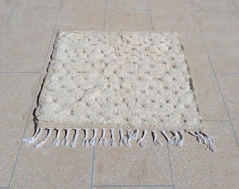May include: A rectangular, off-white rug with a textured surface and a fringe along one edge. The rug has a pattern of small, raised dots and is approximately 24 inches wide and 36 inches long.