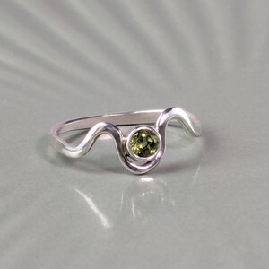May include: A silver ring with a wavy band and a green gemstone in the centre.