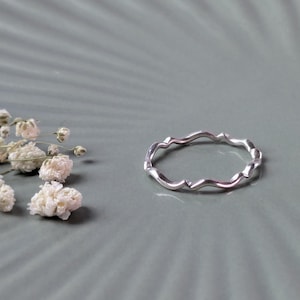 May include: A silver ring with a wavy, organic design. The ring is on a grey background.