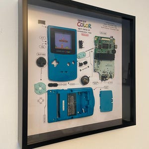 May include: A disassembled teal Game Boy Color with all of its parts laid out on a white background. The parts include the screen, buttons, motherboard, and battery compartment. The text "GAME BOY COLOR GET INTO IT INTRODUCES: 1993" is printed on the white background.