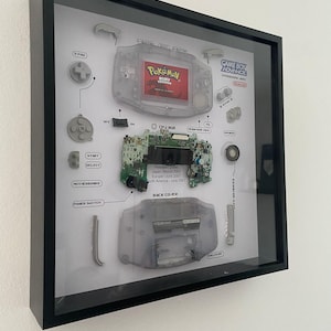 May include: A disassembled Game Boy Advance SP console with all of its parts laid out on a white background. The console is a translucent grey colour and the parts are labelled with their names. The console is a popular handheld gaming device released in 2001.