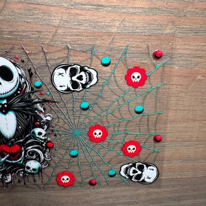 Puede incluir: Una pieza decorativa rectangular transparente con tem&aacute;tica de Halloween. El dise&ntilde;o incluye una telara&ntilde;a con l&iacute;neas turquesas, calaveras rojas con forma de flor, puntos turquesas y rojos, y gr&aacute;ficos de calaveras.