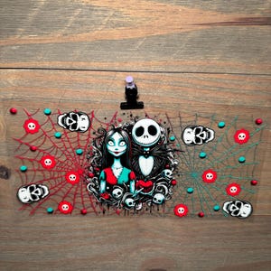 Puede incluir: Un marcap&aacute;ginas transparente de acr&iacute;lico con tem&aacute;tica de Halloween, con Jack Skellington y Sally de Pesadilla antes de Navidad. Presenta telara&ntilde;as rojas y turquesas, motivos de calaveras y una pinza negra.