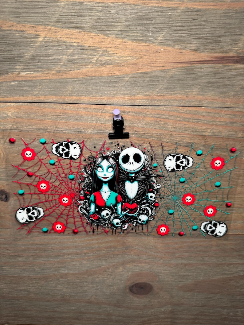 Puede incluir: Un marcap&aacute;ginas transparente de acr&iacute;lico con tem&aacute;tica de Halloween, con Jack Skellington y Sally de Pesadilla antes de Navidad. Presenta telara&ntilde;as rojas y turquesas, motivos de calaveras y una pinza negra.