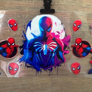 May include: A sheet of Spider-Man themed stickers. The central image is a full-body illustration of Spider-Man in a blue and red suit, set against a white and purple background. Several smaller Spider-Man mask stickers are also visible.