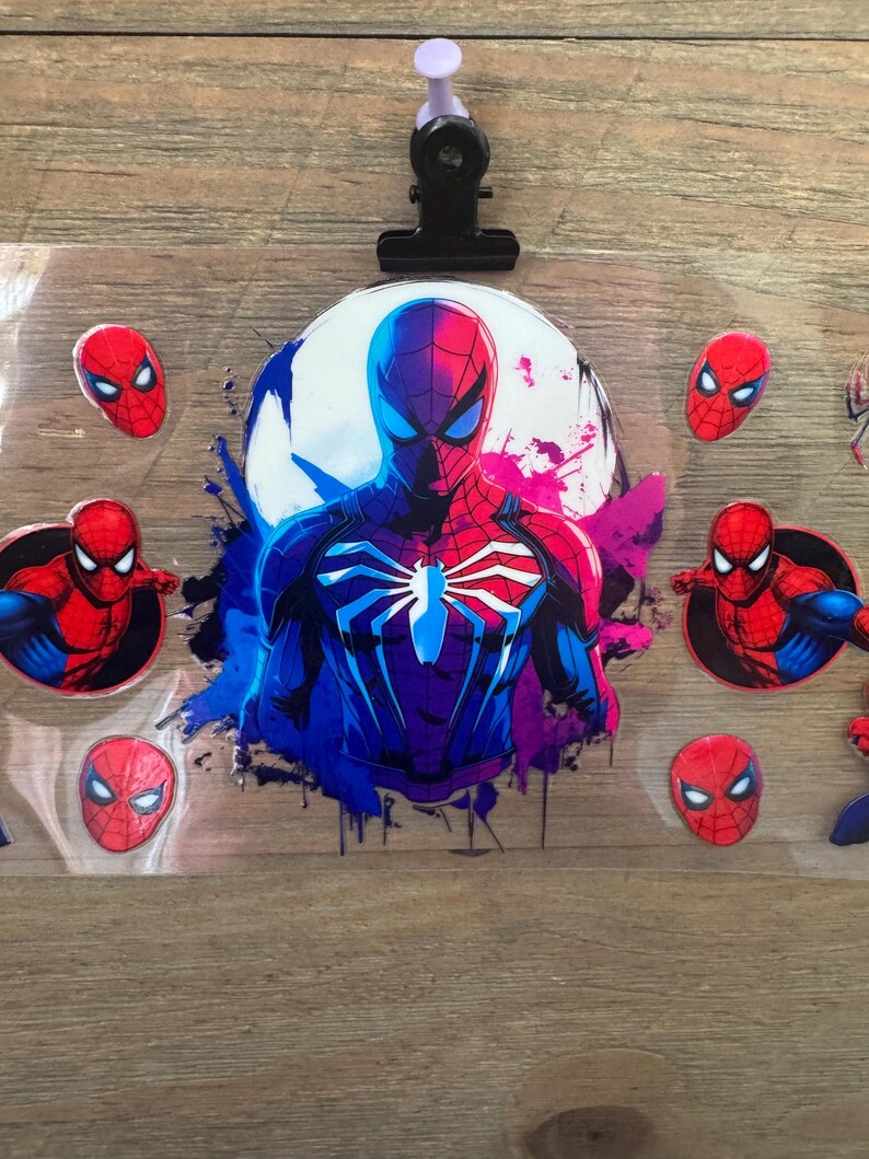 May include: A sheet of Spider-Man themed stickers. The central image is a full-body illustration of Spider-Man in a blue and red suit, set against a white and purple background. Several smaller Spider-Man mask stickers are also visible.