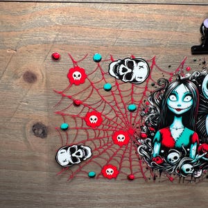 Puede incluir: Un dise&ntilde;o tem&aacute;tico de Halloween con una telara&ntilde;a roja con detalles de calaveras y orbes turquesas. El dise&ntilde;o tambi&eacute;n incluye un personaje con cabello negro, ropa roja y turquesa y un dise&ntilde;o tem&aacute;tico de calaveras. El fondo es una veta de madera.