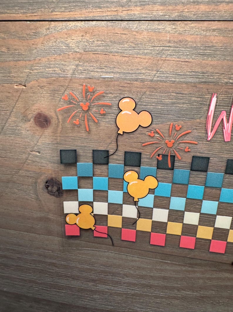 May include: A wooden sign featuring a checkered pattern in rows of black, teal, light blue, white, yellow, and pink squares. Three yellow mouse-shaped balloons and two orange firework designs with small mouse silhouettes are displayed above.