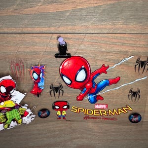 K&ouml;nnte beinhalten: Eine Sammlung von Spider-Man-Aufklebern und Grafiken. Das Hauptbild zeigt einen Cartoon-Spider-Man in einer dynamischen Pose mit den Worten "Marvel Spider-Man Homecoming". Zus&auml;tzliche Aufkleber zeigen Spider-Man-Logos und andere Charakterdesigns.