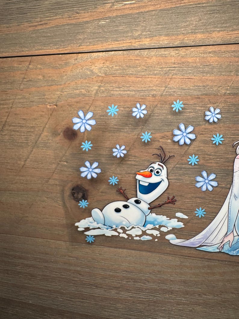 K&ouml;nnte beinhalten: Ein transparenter Aufkleber mit der Figur Olaf aus Die Eisk&ouml;nigin, dargestellt mit einer leuchtend orangefarbenen Karottennase, gro&szlig;en Augen und einem fr&ouml;hlichen Ausdruck, umgeben von zahlreichen hellblauen Schneeflocken-Illustrationen.