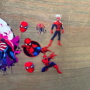 May include: A collection of Spider-Man themed stickers and cutouts. The stickers feature the superhero in various poses, including a full-body figure, a head, and action poses. The color scheme is primarily red, blue, and black.