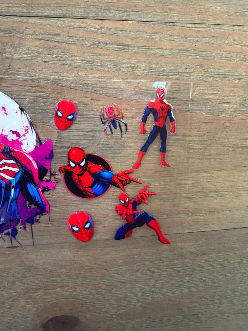 May include: A collection of Spider-Man themed stickers and cutouts. The stickers feature the superhero in various poses, including a full-body figure, a head, and action poses. The color scheme is primarily red, blue, and black.