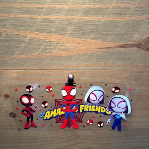 May include: A clear transfer sheet featuring cartoon characters from Spidey and His Amazing Friends, including Miles Morales, Peter Parker, and Ghost-Spider, with red spider web accents, small black stars, and the yellow text "and his AMAZING FRIENDS."