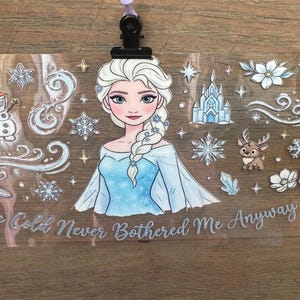 May include: A clear sticker featuring a cartoon illustration of a princess with white hair and a blue dress. The sticker includes snowflakes, a castle, and the text "The Cold Never Bothered Me Anyway."