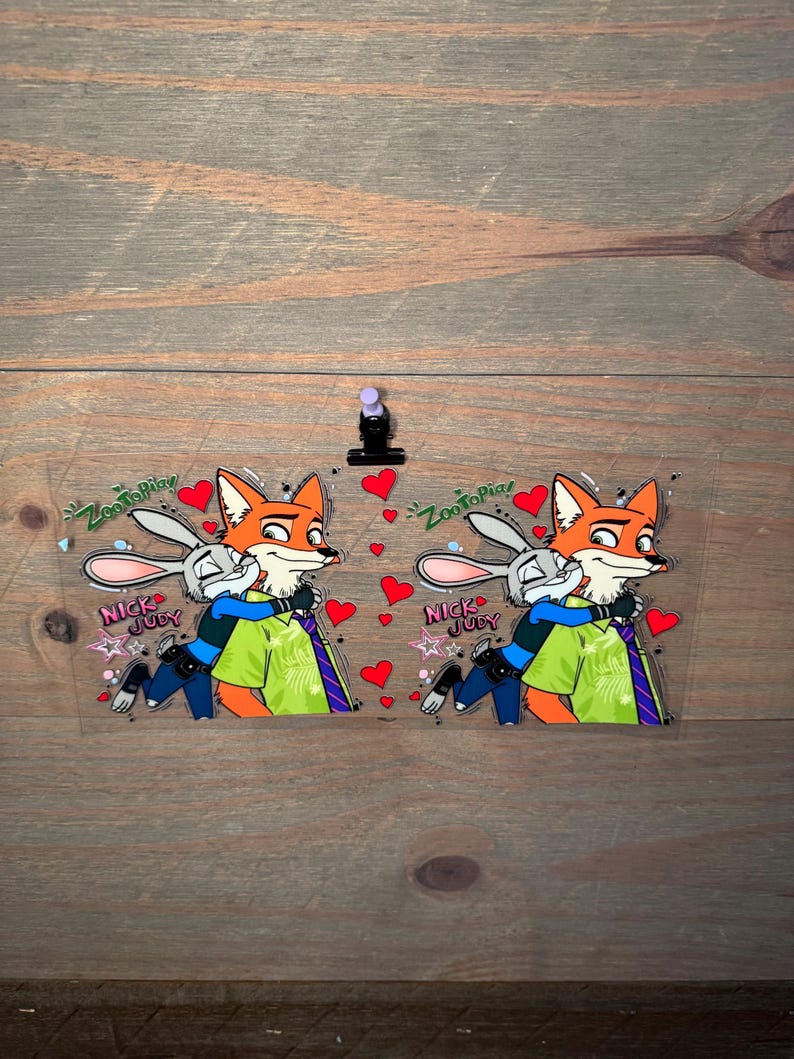 May include: Two clear acrylic charms featuring Nick Wilde and Judy Hopps from Zootopia. The fox and bunny characters are hugging, surrounded by red hearts. Text includes "Zootopia" and "Nick & Judy".