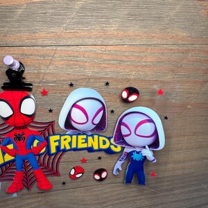 May include: A clear plastic sheet featuring cartoon character stickers including a red and blue spider-themed hero, a white and purple hooded character, and the yellow text FRIENDS. The design includes small red stars, black stars, and spider mask icons.