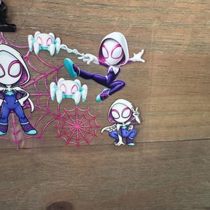 May include: A collection of Spider-Gwen character cutouts in various poses. The figures are primarily purple, white, and blue, with spider web and spider accents. One figure is mid-air, attached to a web.