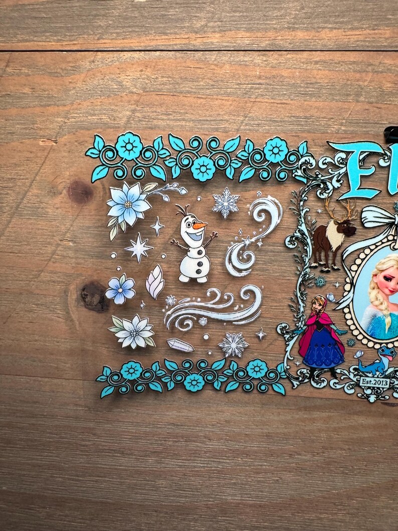 Puede incluir: Una l&aacute;mina de pegatinas transparente con personajes y elementos de la pel&iacute;cula "Frozen". El dise&ntilde;o incluye im&aacute;genes de Olaf, Elsa, Anna, copos de nieve y detalles florales en tonos azules y blancos. El texto "Frozen" es visible.