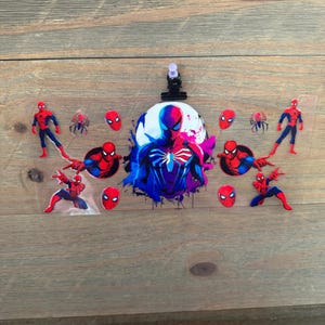 May include: A clear plastic sheet featuring various Spider-Man graphics. The design includes multiple Spider-Man figures in red and blue, along with spider emblems and Spider-Man's mask. A black clip is attached at the top.