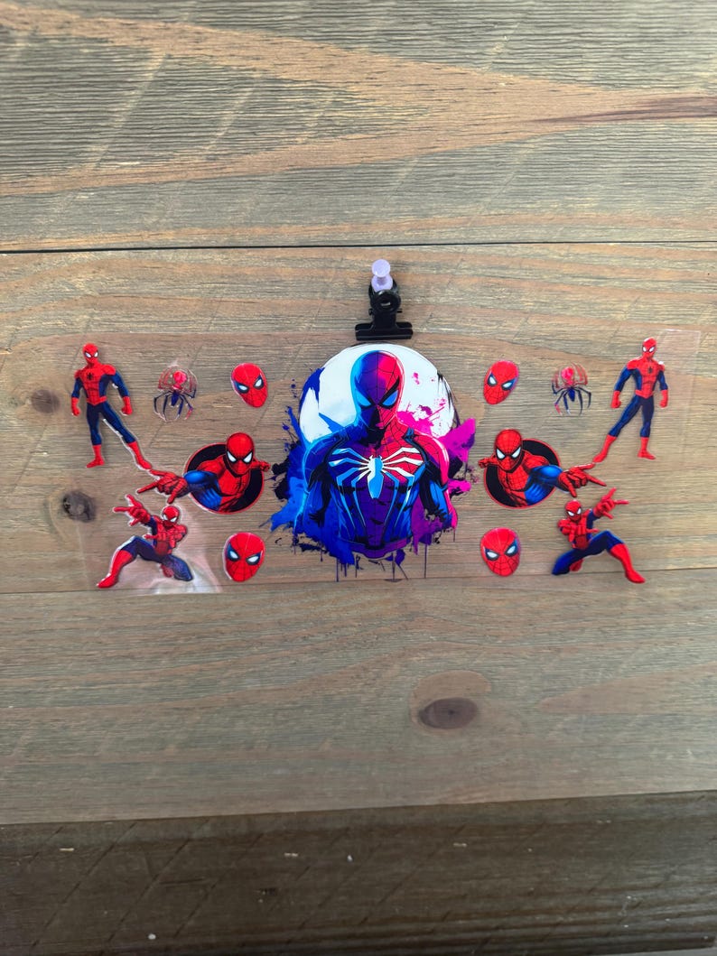 May include: A clear plastic sheet featuring various Spider-Man graphics. The design includes multiple Spider-Man figures in red and blue, along with spider emblems and Spider-Man's mask. A black clip is attached at the top.