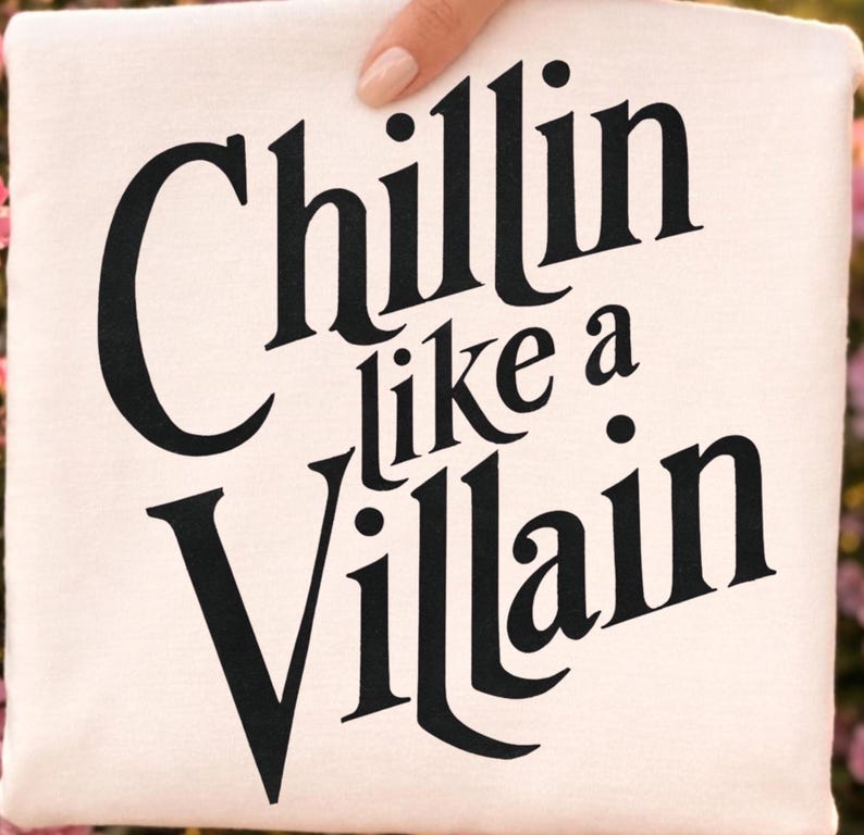 Puede incluir: Una camiseta de color crema con el texto negro "Chillin like a Villain" impreso en una fuente serif audaz y estilizada. El dise&ntilde;o est&aacute; centrado en la parte delantera de la prenda, con las palabras dispuestas en tres l&iacute;neas distintas sobre la tela.