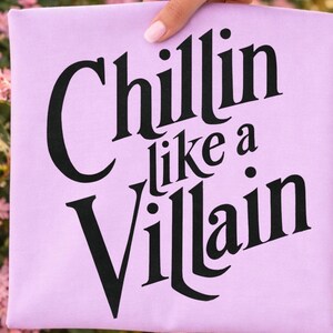 Puede incluir: Una camiseta de color morado claro con el texto negro "Chillin like a Villain" impreso en una fuente serif negrita y estilizada. Las letras est&aacute;n dispuestas en tres l&iacute;neas, con la palabra "Chillin" arriba, "like a" en el medio y "Villain" abajo.