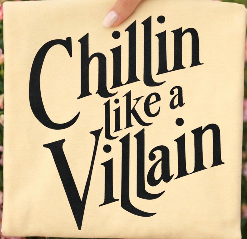 Puede incluir: Una camiseta de color crema claro con texto negro en negrita que dice "Chillin like a Villain" en una fuente serif estilizada. Las letras est&aacute;n centradas en la tela, con la palabra "Chillin" en la parte superior, "like a" en el medio y "Villain" debajo.
