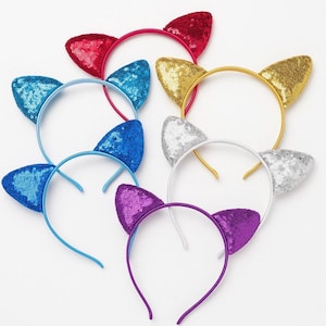 May include: A selection of sequined cat ear headbands in a range of colours: red, blue, gold, silver, and purple. Each headband has a matching coloured band and ears, ideal for costumes or themed events.