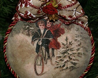 May include: A vintage-style Christmas bauble featuring a red and gold bow with a floral accent. The bauble depicts two children riding a bicycle in a snowy winter scene.
