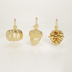 Puede incluir: Tres colgantes dorados con forma de calabaza, bellota y piña. Cada colgante tiene un lazo en la parte superior para sujetarlo a un collar o pulsera. Los colgantes son muy detallados y reflejan la luz.