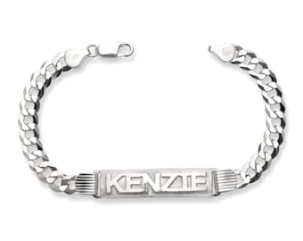May include: A silver curb chain bracelet with the name "KENZIE" engraved on a rectangular plate. The bracelet has a lobster clasp closure and is displayed against a white background.