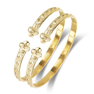May include: Two gold-colored bangle bracelets with a decorative, patterned design. The bracelets are open and have a rounded end.