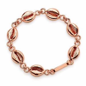 May include: A rose gold-toned bracelet featuring seven metallic cowrie shell charms linked together by circular rings, with a smooth rectangular bar element integrated into the chain structure to complete the circular design.