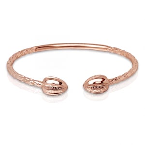Könnte beinhalten: Roségoldener Armreif mit strukturierter Band und dekorativen Enden. Das Armband hat eine gehämmerten Textur auf dem Band und detaillierte, ovale Endstücke. Das offene Design ermöglicht ein einfaches Tragen. Ein stilvolles Schmuckaccessoire.