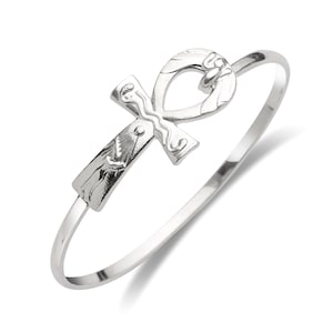 May include: A silver bangle bracelet with an ankh symbol charm. The ankh is a stylized cross with a loop at the top.
