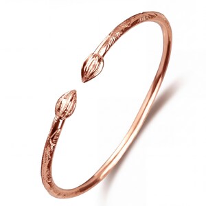 Könnte beinhalten: Roségoldfarbenes Armreif-Armband mit floralen und Blattdetails. Das offene Design hat zwei stilisierte Lotusknospen-Terminals. Das Armband hat eine glatte, polierte Oberfläche und ist vor weißem Hintergrund platziert.