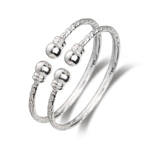 May include: Two silver-colored, open-ended bangles. Each bangle has a textured band and features two decorative ball-shaped accents. The ends of the bangles are slightly curved, creating an adjustable fit. The jewelry is displayed against a white background.
