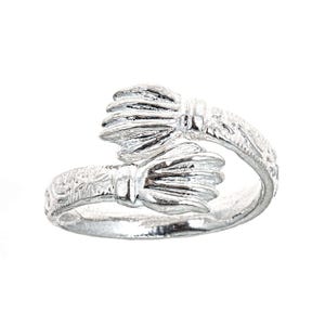 May include: A silver ring with a delicate design featuring two stylized floral motifs. The ring is made of sterling silver and has a polished finish.