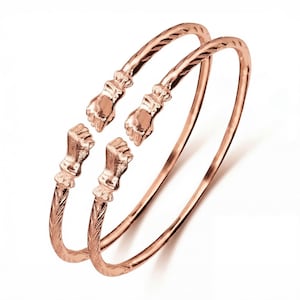 Könnte beinhalten: Zwei roségoldfarbene Armreifen. Jeder Armreif hat einen handförmigen Verschluss an der Öffnung. Einer hat ein strukturiertes Design am Arm, der andere ist glatt. Die Armreifen werden auf weißem Hintergrund präsentiert.