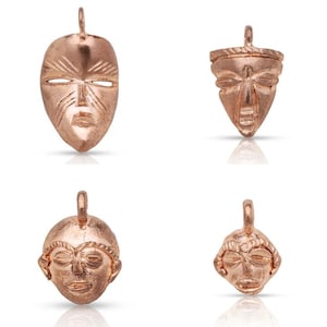 May include: Four rose gold colored metal charms in the shape of African masks. The masks have different facial features and designs.