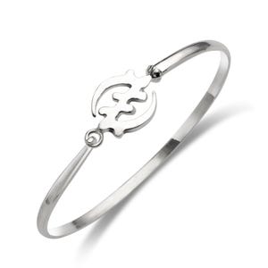 May include: A silver-colored bangle bracelet with a decorative Adinkra symbol in the center. The bracelet has a hinged design and a polished finish. The Adinkra symbol is a stylized representation of a concept or proverb.