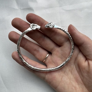 May include: Silver bracelet with ram's head accents. The bracelet is detailed with a textured design.