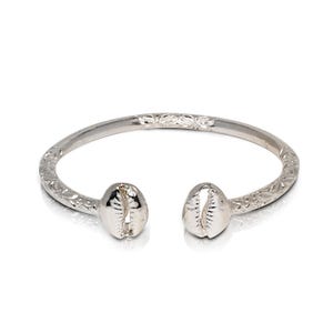 May include: Silver bangle bracelet with a detailed etched design and cowrie shell accents.