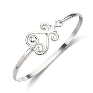 May include: A silver-colored bangle bracelet with a decorative heart-shaped design. The heart features swirling patterns and is connected to the bracelet's clasp. The bracelet is made of a shiny, reflective metal.