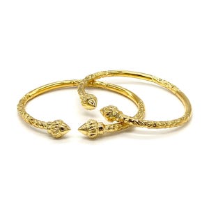 May include: Two gold-toned open bangles featuring a textured surface and pointed, cone-shaped finials at each end. The metal surface of the bracelets displays a repeating, intricate pattern along the entire length of the circular bands.