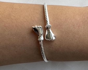 May include: A silver bracelet with two hand-shaped charms. The bracelet is made of a textured metal and has a simple design.
