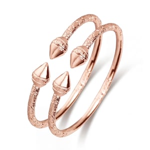 Könnte beinhalten: Roségoldfarbener Ring mit einzigartigem Design. Der Ring hat drei Bänder mit strukturierten Details und konisch geformten Akzenten. Der Schmuck wird auf weißem Hintergrund präsentiert, um seine komplizierten Details und das metallische Finish hervorzuheben.